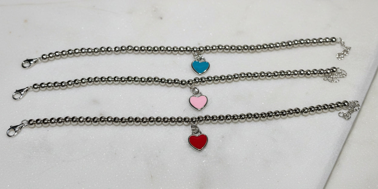 Three silver bracelets with heart-shaped charms on a light surface
