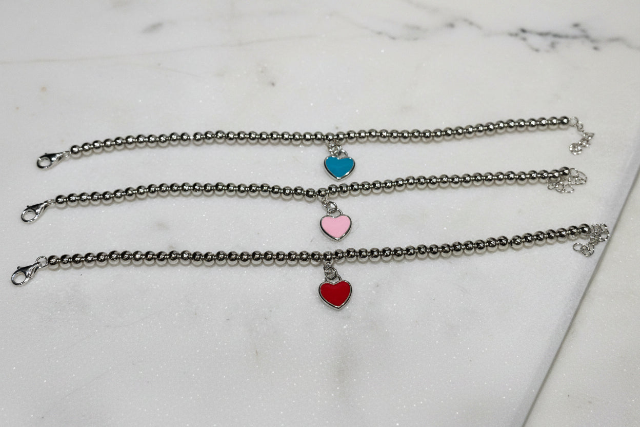 Three silver bracelets with heart-shaped charms on a light surface