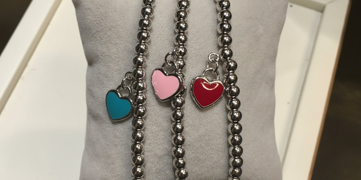 Three silver beaded bracelets with colorful heart charms held on a light gray surface.