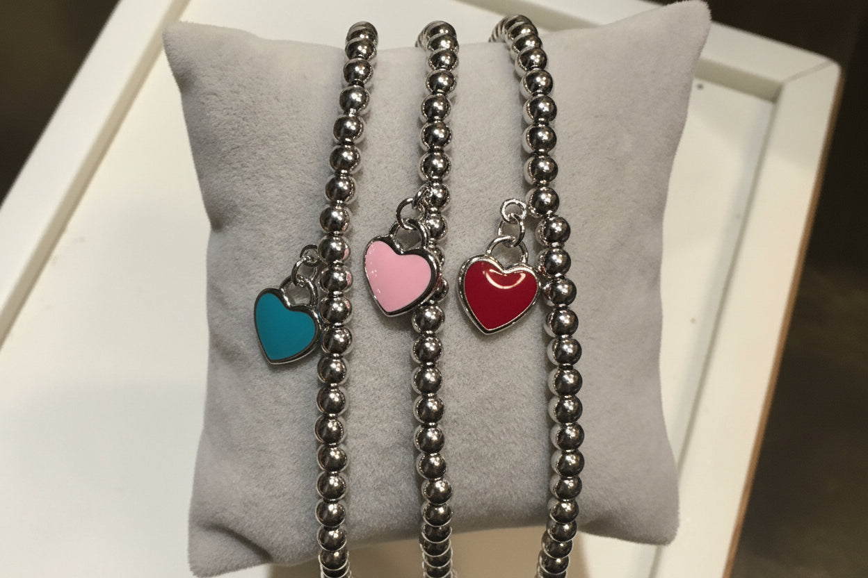 Three silver beaded bracelets with colorful heart charms held on a light gray surface.