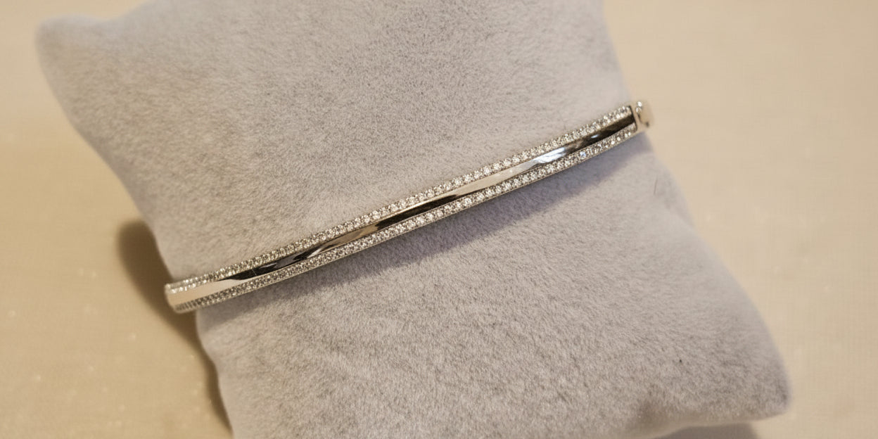 A bracelet with cubic zirconia stones set in a gold or rhodium-filled band, displayed on a grey velvet surface.