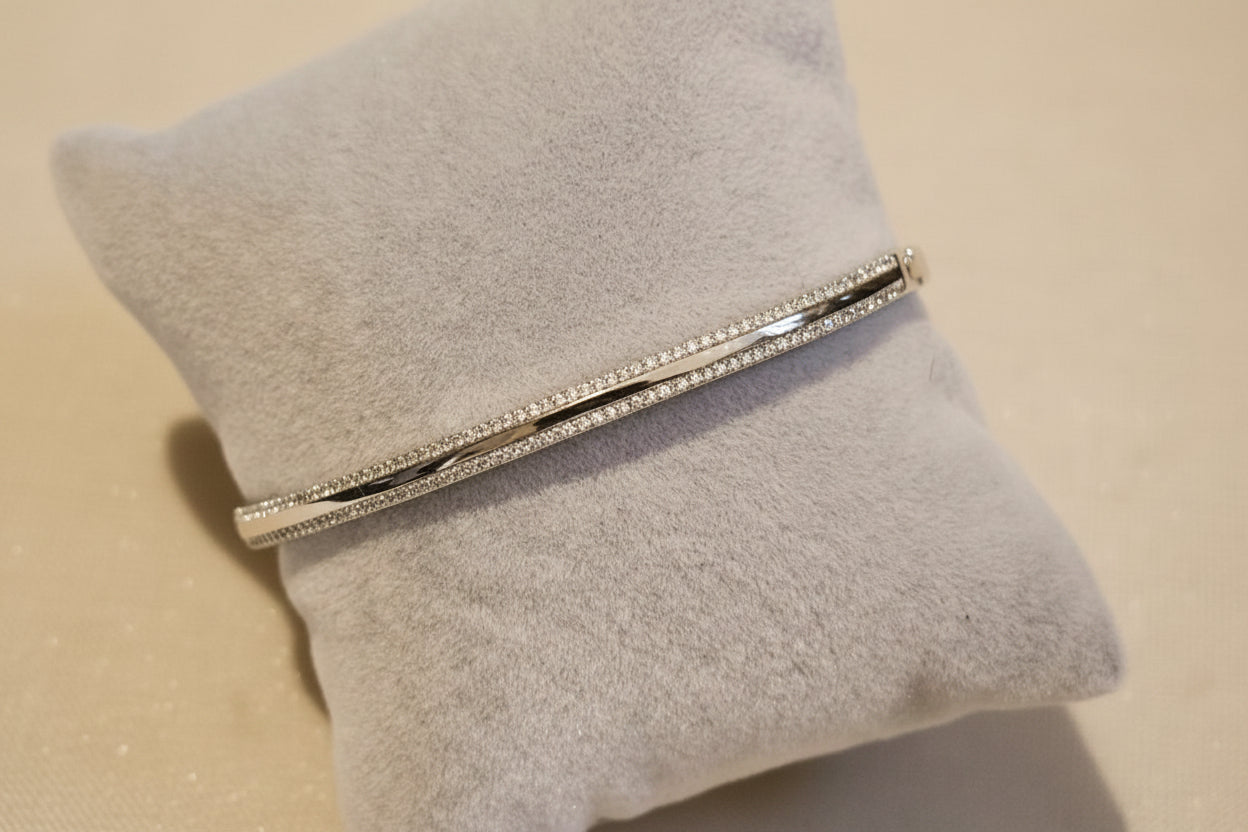 A bracelet with cubic zirconia stones set in a gold or rhodium-filled band, displayed on a grey velvet surface.