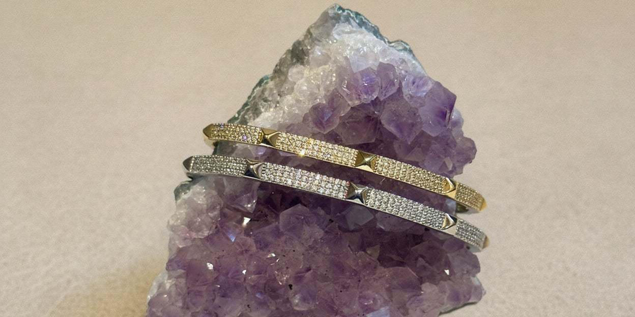 A gold bangle bracelet with pave studs, resting on a purple crystal.