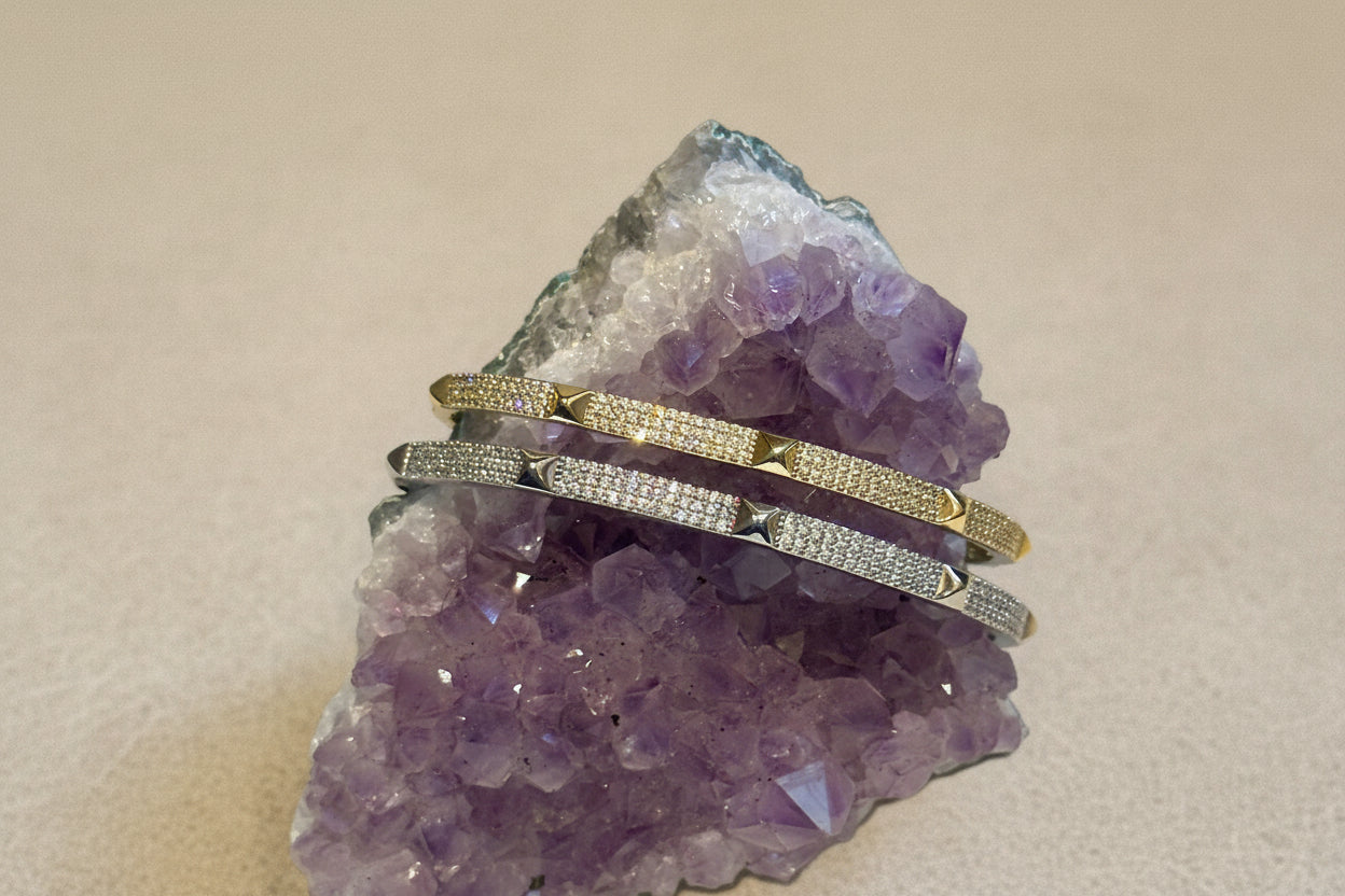 A gold bangle bracelet with pave studs, resting on a purple crystal.