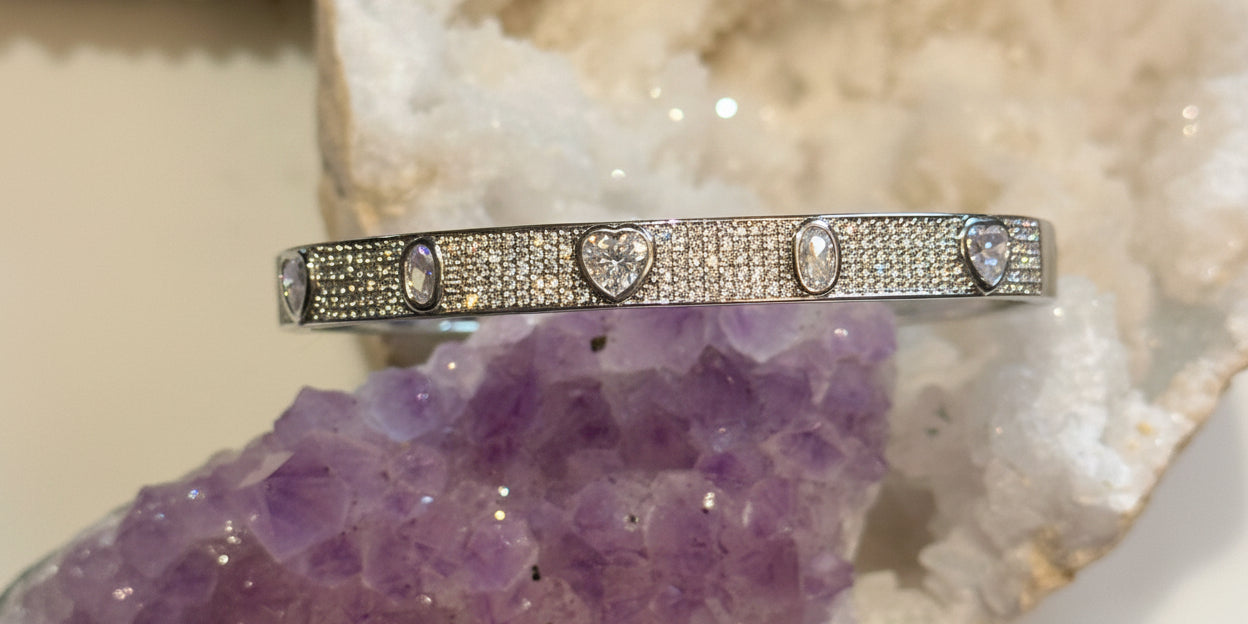 A multi-stone pave bangle bracelet with a gold and rhodium filled band, set with diamonds, positioned on a purple crystal.