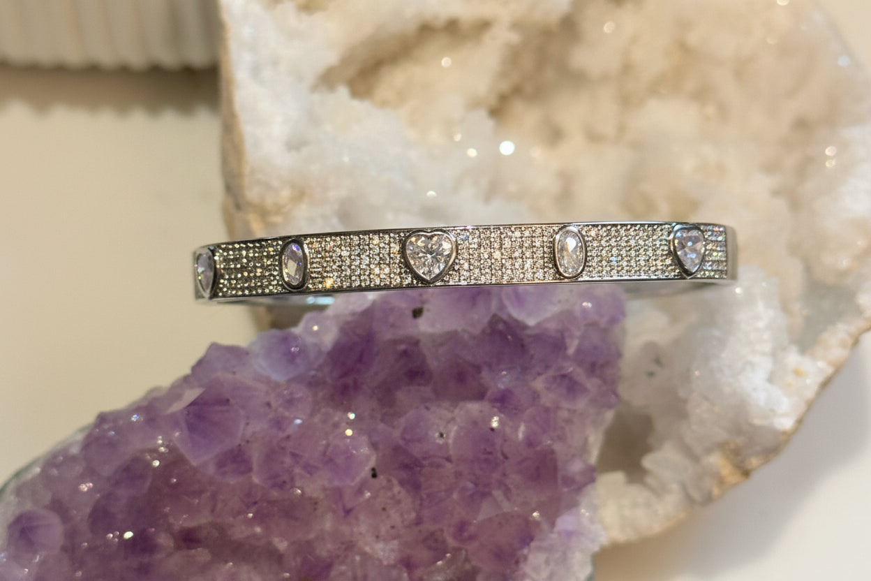 A multi-stone pave bangle bracelet with a gold and rhodium filled band, set with diamonds, positioned on a purple crystal.