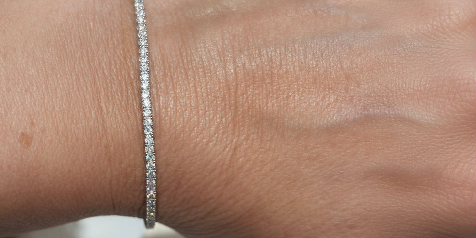 A person wearing a white watch is showcasing a silver bangle bracelet adorned with cubic zirconia stones on their wrist.