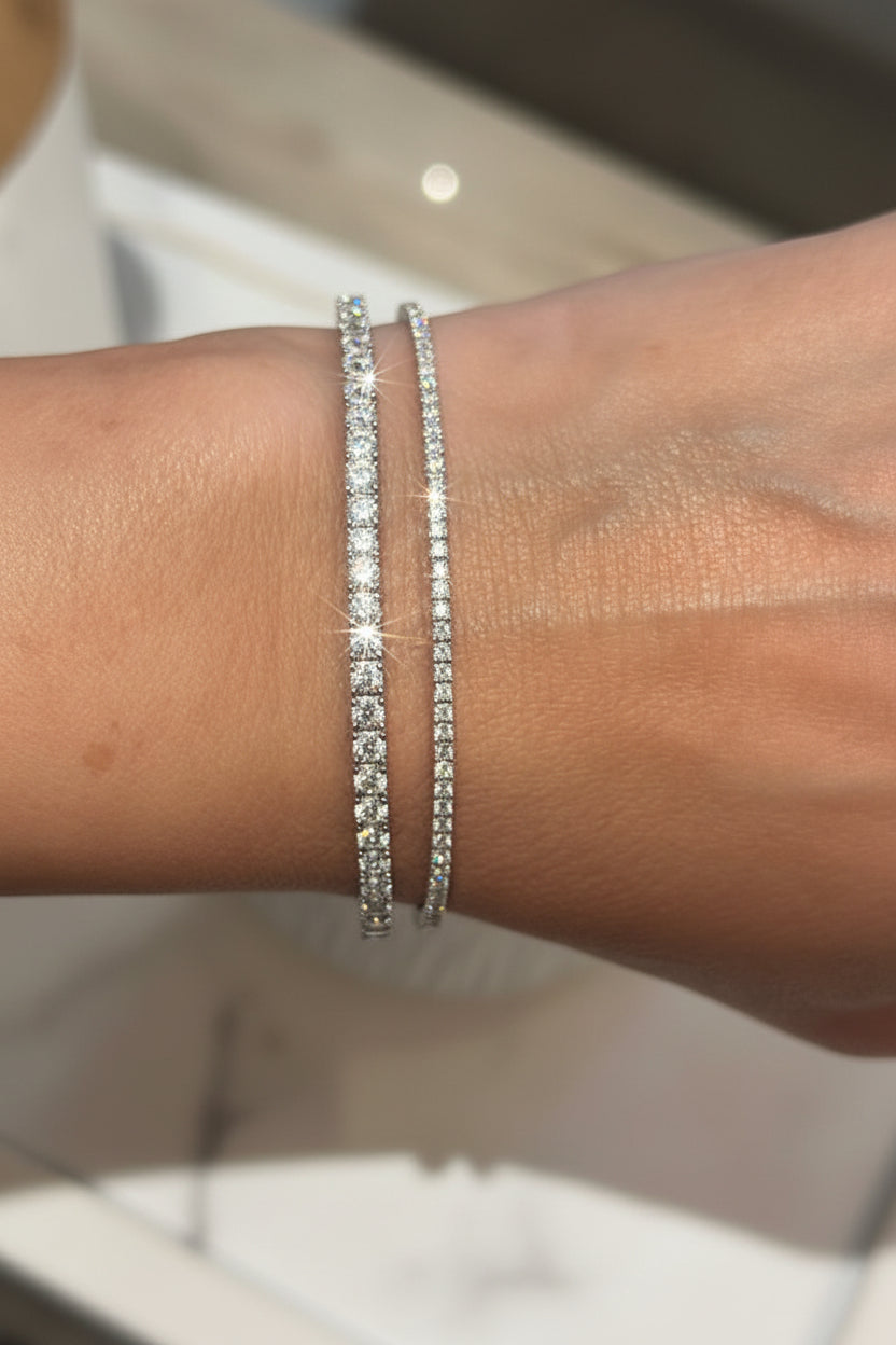 Close-up of a wrist wearing two silver bracelets with a blurred green plant background