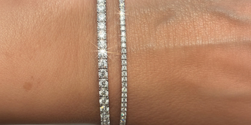 Close-up of a wrist wearing two silver bracelets with a blurred green plant background