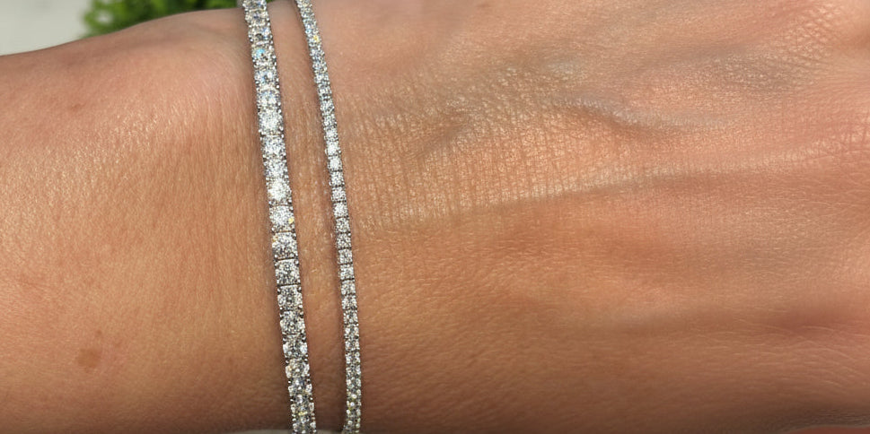 Close-up of a wrist wearing two silver bracelets with a blurred green plant background