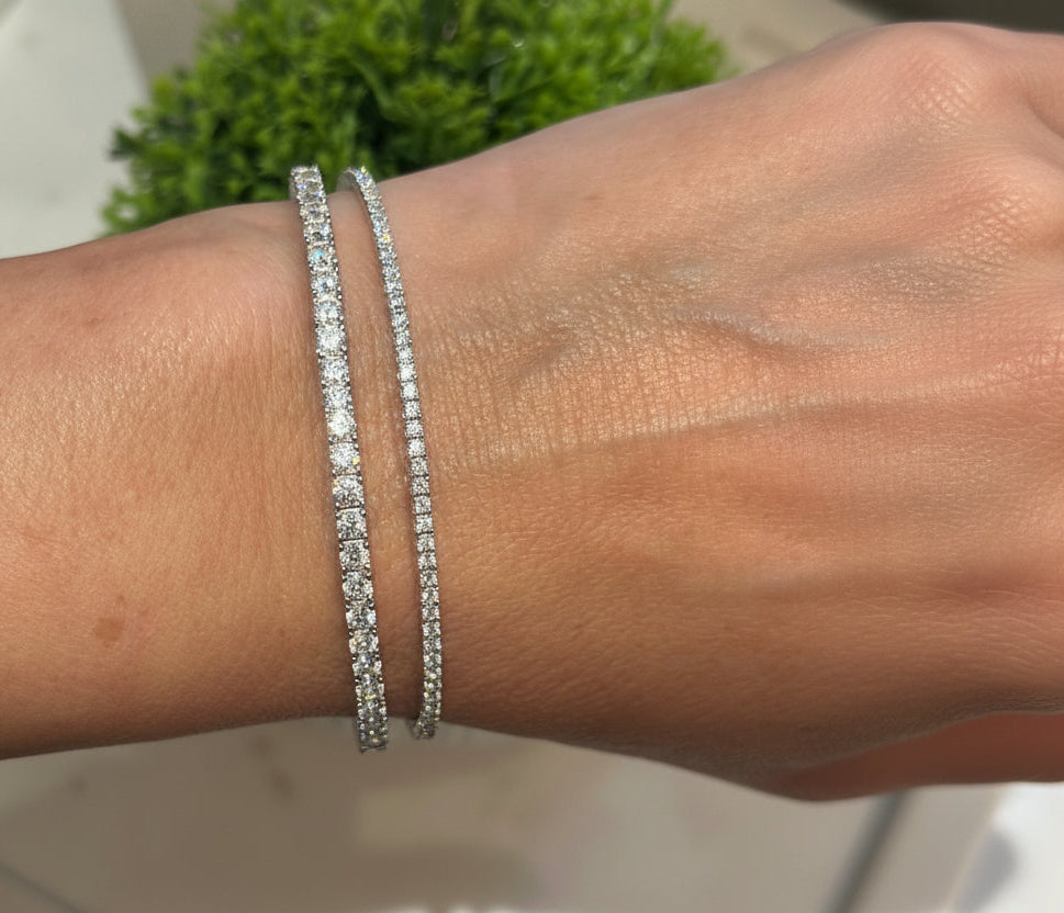 Close-up of a wrist wearing two silver bracelets with a blurred green plant background