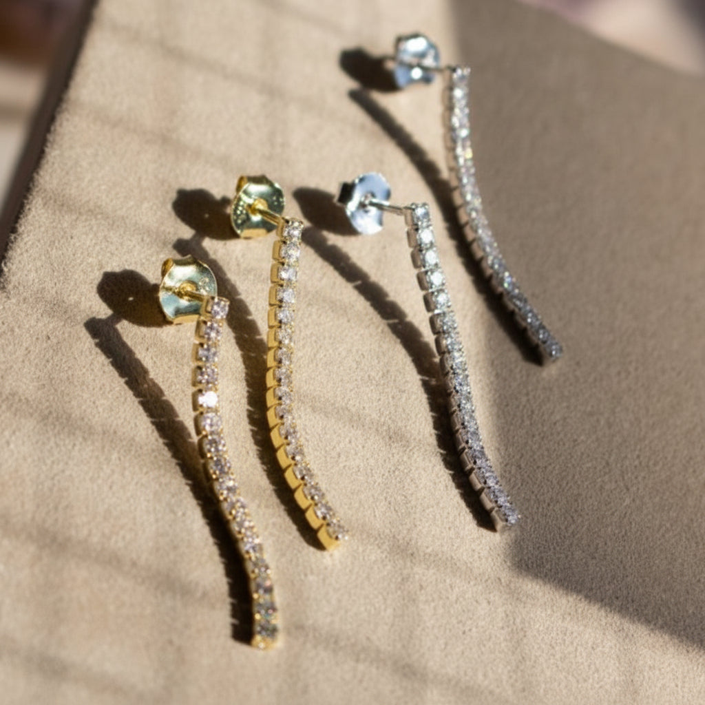 A pair of tennis drop earrings with yellow and white stones set in gold-tone mountings, displayed on a textured surface.