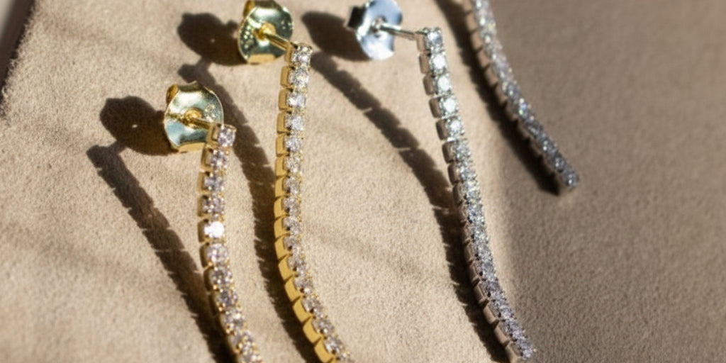 A pair of tennis drop earrings with yellow and white stones set in gold-tone mountings, displayed on a textured surface.