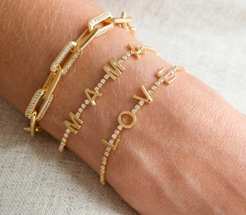 Gold bracelets with 'I love you' on a wrist against a neutral background