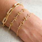 Gold bracelets with 'I love you' on a wrist against a neutral background